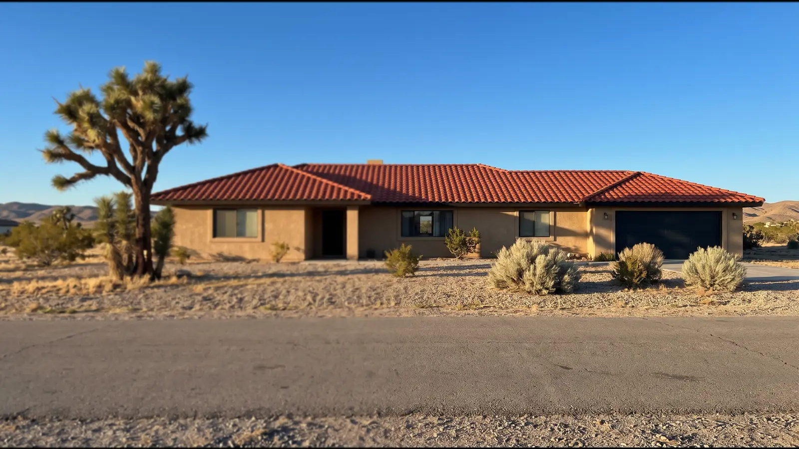 Single-story stucco ranch house with a red concrete S-tile roof and a Joshua tree in the gravel front yard