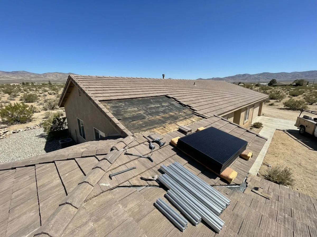 Solar panels unbolted and stacked on padded blocks beside a concrete tile roof with the underlayment exposed